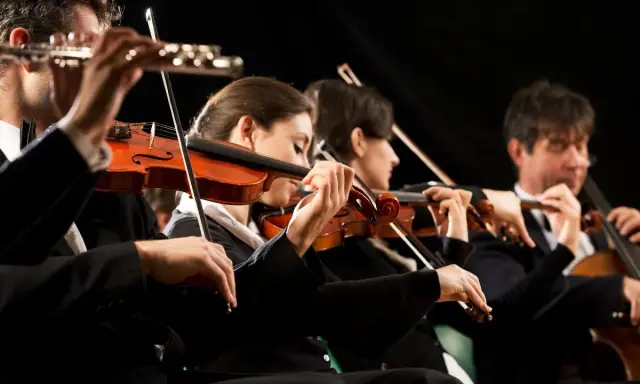 Orkiestra wykonuje utwór jednego z kompozytorów XX wieku. Skupieni muzycy grają na skrzypcach i wiolonczeli.
