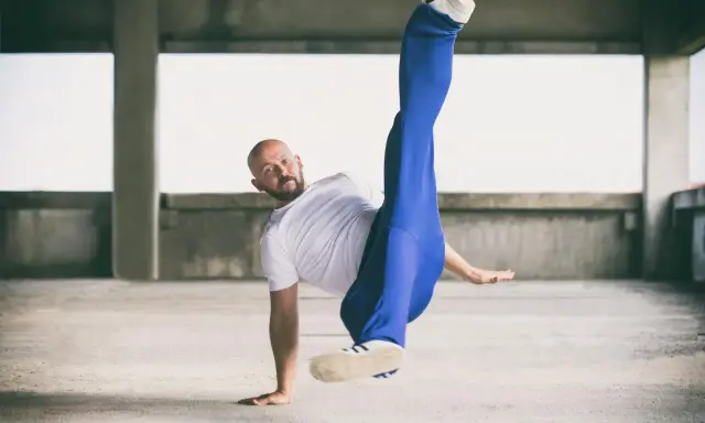 Mężczyzna w białej koszulce i niebieskich spodniach wykonuje akrobatyczny ruch. Czy to może być odpowiedź na pytanie: beatbox co to?