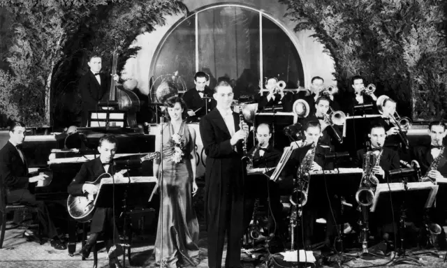 Orkiestra grająca muzykę lat 30. na scenie. Wokalistka w eleganckiej sukni, klarnetysta, gitarzysta i sekcja dęta.