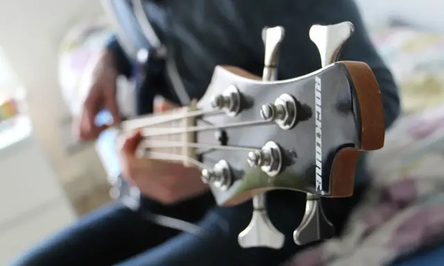 Osoba gra na gitarze basowej, tworząc głębokie akordy basowe.