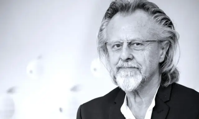 Portret mężczyzny z siwą brodą i długimi włosami, w okularach. Jeden z najlepsi współcześni kompozytorzy.