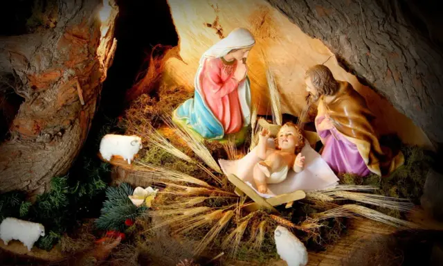 Szopka z figurkami Maryi, Józefa i Dzieciątka Jezus. Owce i kłosy zbóż dopełniają scenę, przypominając o historii kolęd.