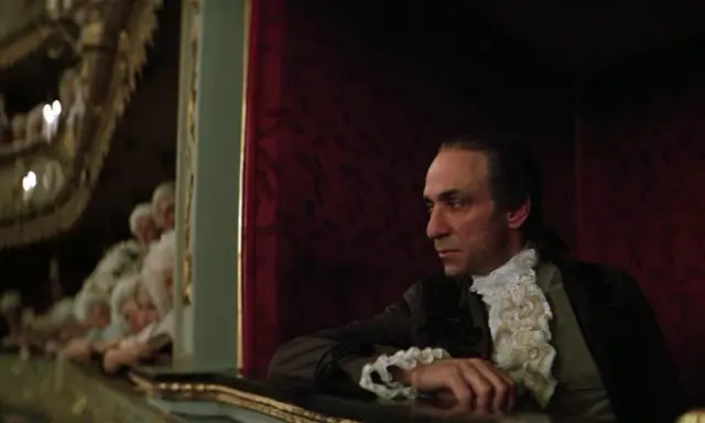 Scena z filmu o Mozarcie. Mężczyzna w stroju z epoki, w loży teatralnej, z widownią w tle.