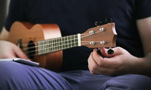 Osoba stroi ukulele, korzystając z aplikacji do nauki gry.