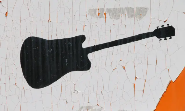 Czarna sylwetka gitary elektrycznej na białym, popękanym tle. Wyobraź sobie rockowy koncert i wirtuoza grającego na tym instrumencie.