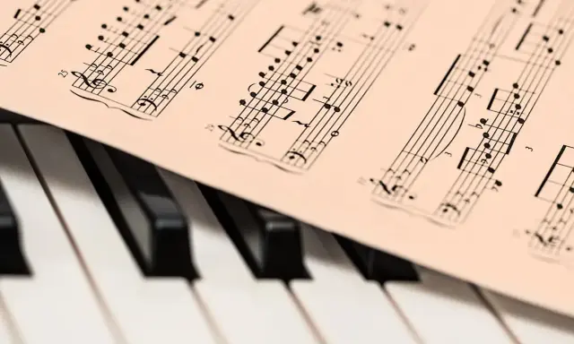 Partytura muzyczna na klawiaturze pianina. Widoczne nuty i klucze, które oddają bogate **cechy muzyki barokowej**.