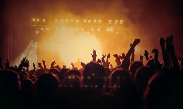 Tłum ludzi z rękami w górze, świętujący koncert. W tle scena z oświetleniem, tworząca atmosferę amerykańskiego stylu w muzyce.