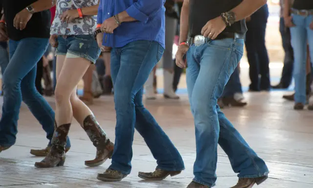 Ludzie w dżinsach i kowbojkach tańczą w rytm amerykańskiego country.