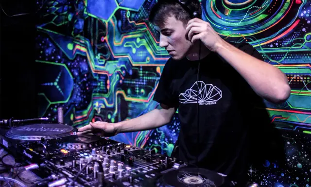 Młody DJ w słuchawkach miksuje muzykę na tle psychodelicznej, neonowej ściany. Chcesz wiedzieć, jak zostać DJ-em? Zacznij od tego!