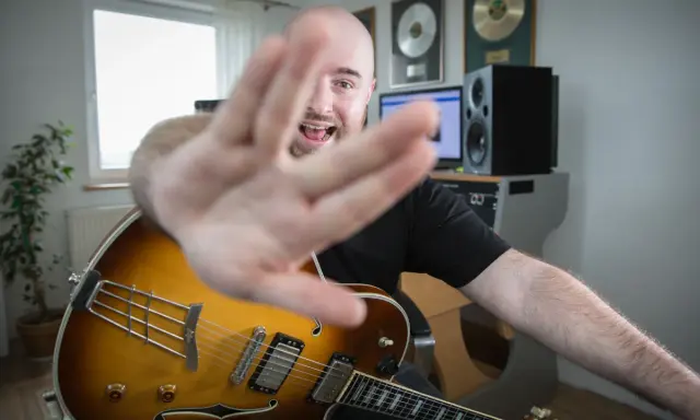 Muzyk z gitarą jazzową, z ręką na pierwszym planie, śpiewa, wyjaśniając, akord co to.
