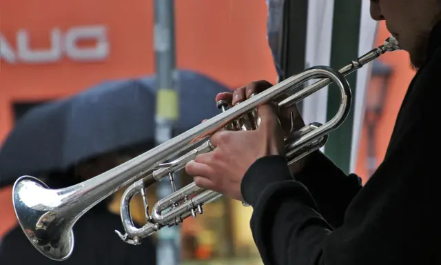 Muzyk gra na trąbce, tworząc dźwięki blues muzyka. W tle deszcz i parasol.