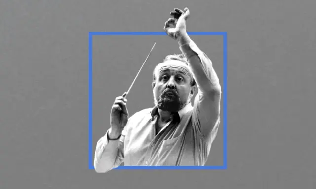 Krzysztof Penderecki, dyrygent z batutą w dłoni, w skupieniu prowadzi orkiestrę.
