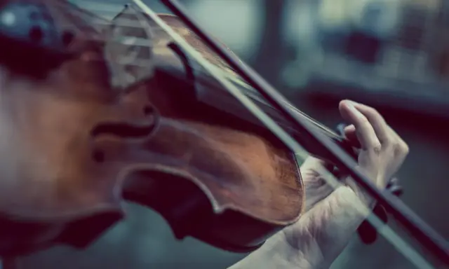 Dłoń gra na skrzypcach Stradivarius, wydobywając z nich magiczne dźwięki.