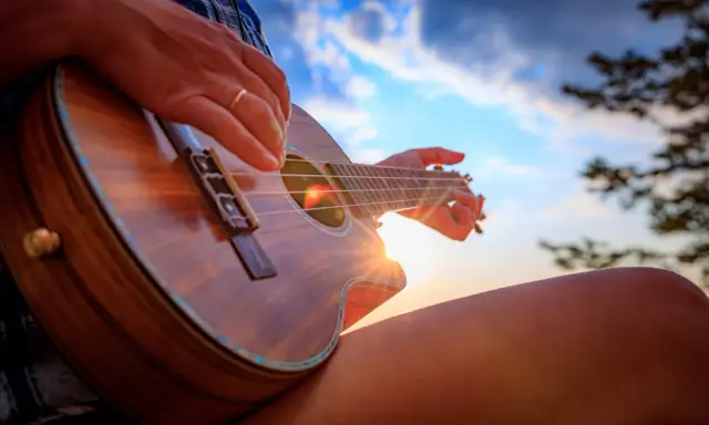 Dłoń z pierścionkiem pokazuje, jak trzymać ukulele, grając przy zachodzącym słońcu.