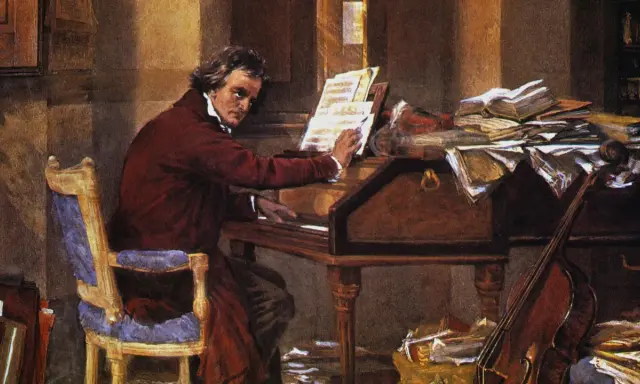 Beethoven, który kompozytor był głuchy, siedzi przy fortepianie, otoczony nutami i książkami.