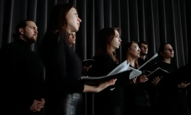 Chór w czarnych strojach, z nutami w rękach. Słychać głosy męskie i kobiece, tworzące harmonijną całość.