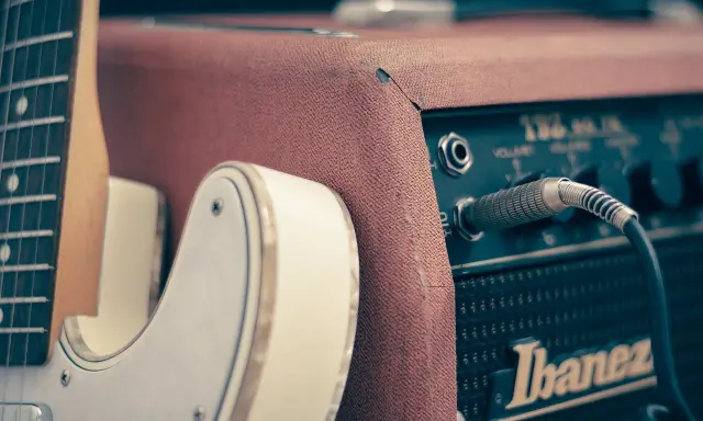 Biała gitara elektryczna podłączona do wzmacniacza Ibanez. Idealny zestaw, by zacząć naukę, jak grać na gitarze elektrycznej.