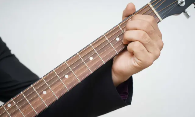Dłoń dociska struny na gryfie gitary, pokazując pierwszy krok, jak nauczyć się grać na gitarze.