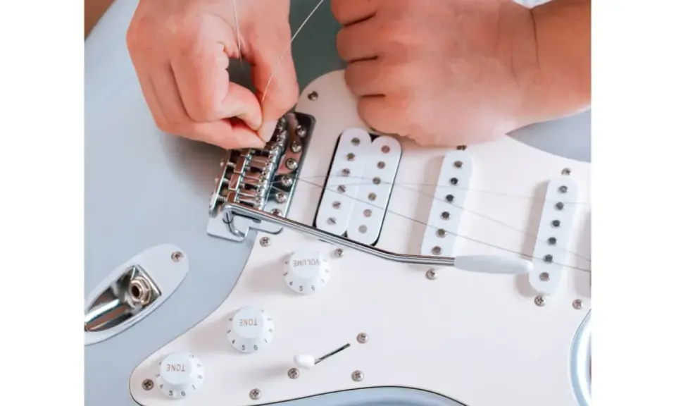 Ręce montują struny do mostka gitary elektrycznej. To ważny krok, jak zrobić gitarę elektryczną, by brzmiała idealnie.