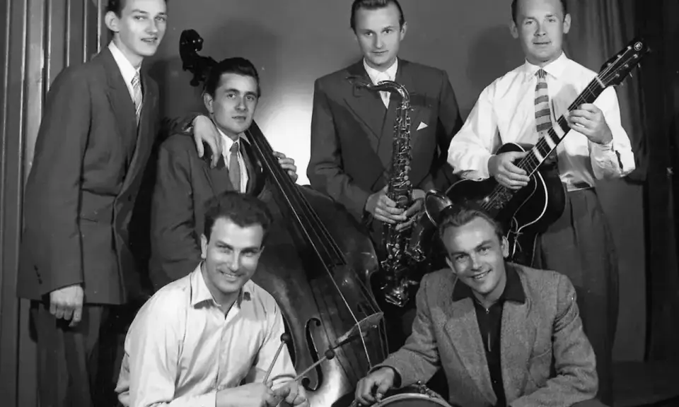 Zespół młodych muzyków, być może najsłynniejsi przedstawiciele jazzu, pozuje z instrumentami: kontrabasem, saksofonem, gitarą i perkusją.
