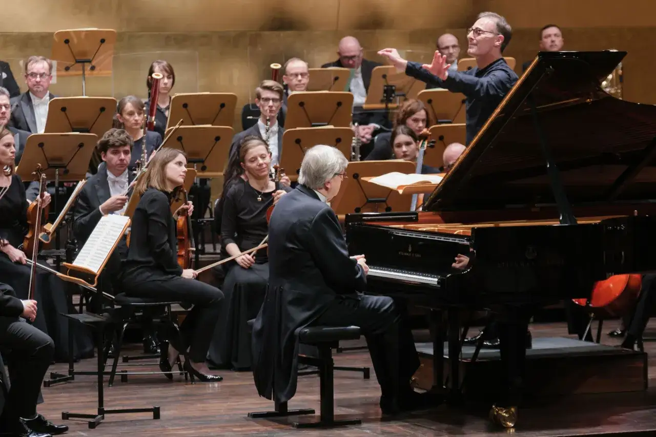 Dyrygent kieruje orkiestrą, a pianista, twórca muzyki, gra na fortepianie.