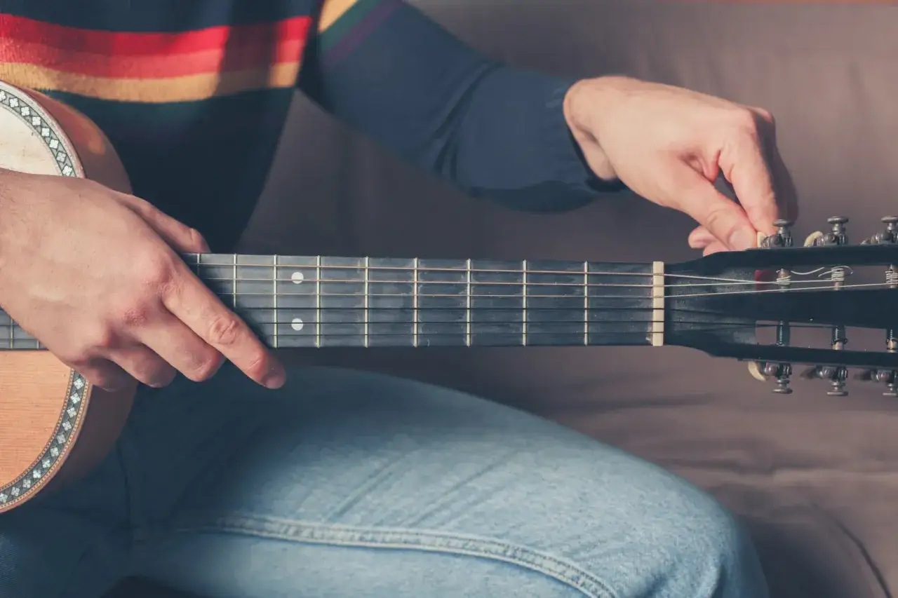 Ręka kręci kluczem, by nastroić gitarę klasyczną. Dźwięki zaraz będą idealne.