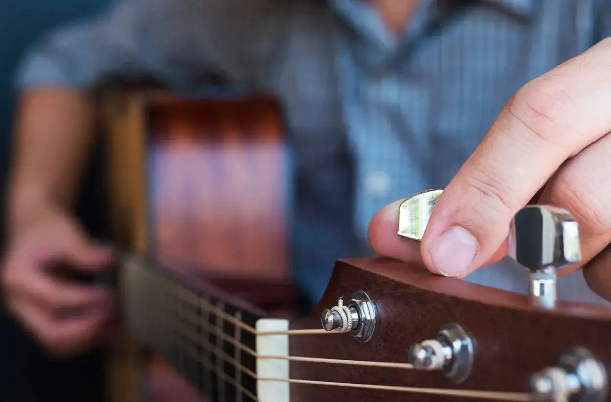 Dłoń stroi gitarę, kręcąc kluczem, by uzyskać idealny dźwięk e.