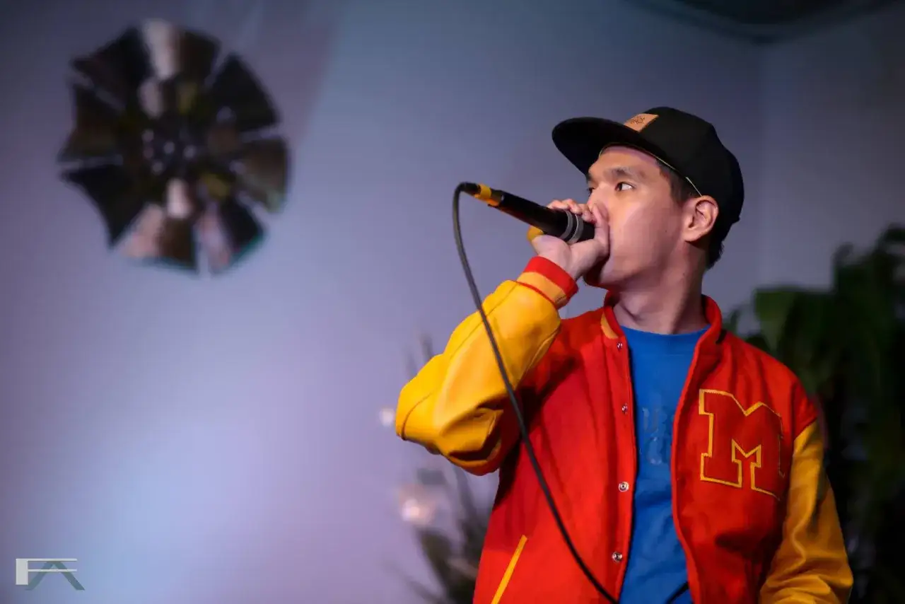 Mężczyzna w czapce i kurtce z literą M wykonuje beatbox. To sztuka tworzenia dźwięków muzycznych ustami.