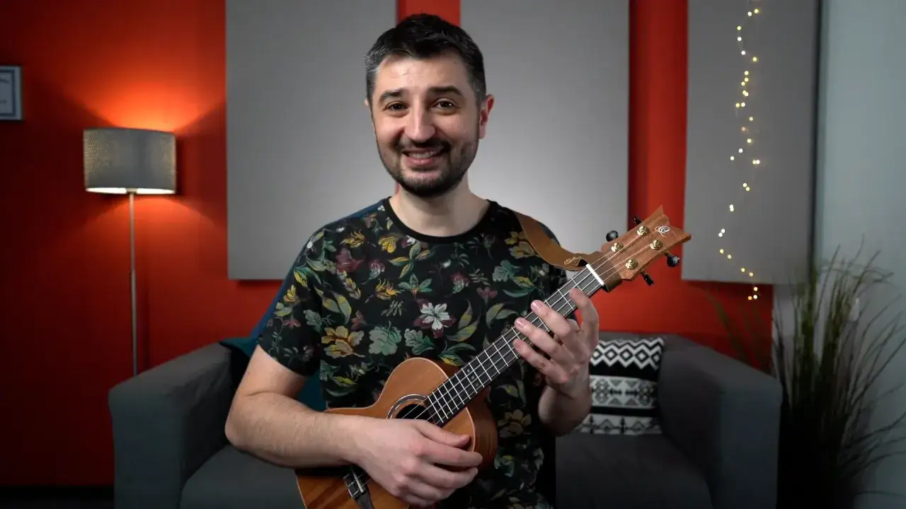 Uśmiechnięty mężczyzna z ukulele w dłoniach. Czy gra na ukulele jest trudna? Ten instrument wygląda na prosty w obsłudze.