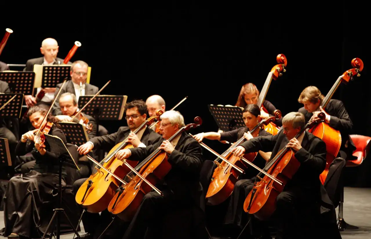Orkiestra grająca czeską muzykę. Skrzypkowie i wiolonczeliści w czarnych strojach na scenie.