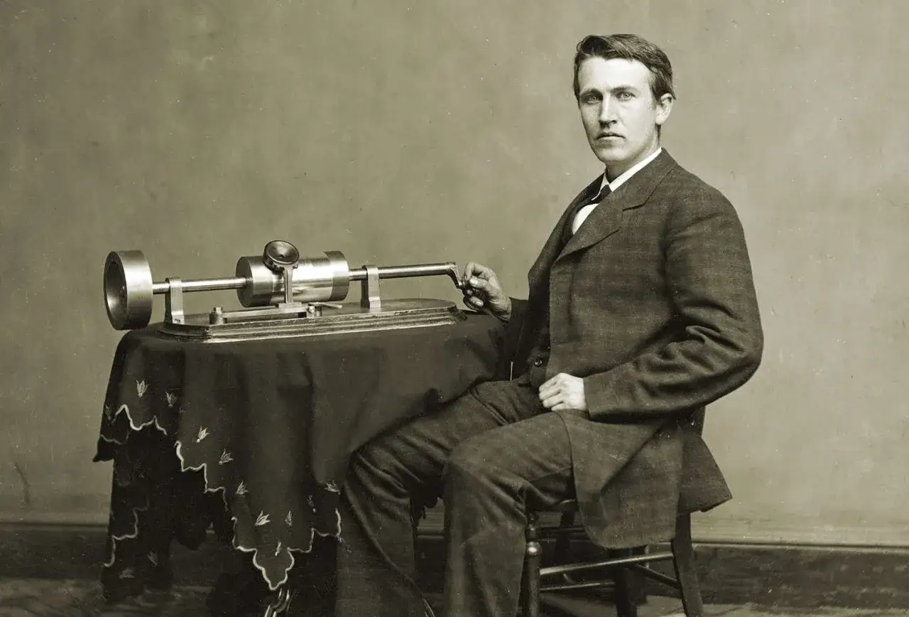 Thomas Edison siedzi obok swojego wynalazku, fonografu.