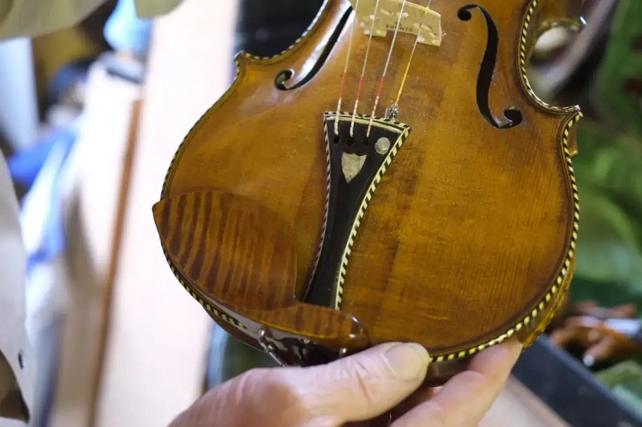 Dłoń trzyma fragment zabytkowych skrzypiec Stradivarius, ukazując ich piękno i mistrzostwo wykonania.