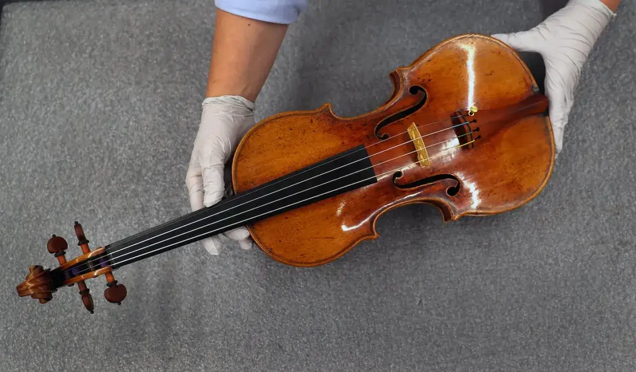 Ręce w białych rękawiczkach trzymają zabytkowy stradivarius instrument.