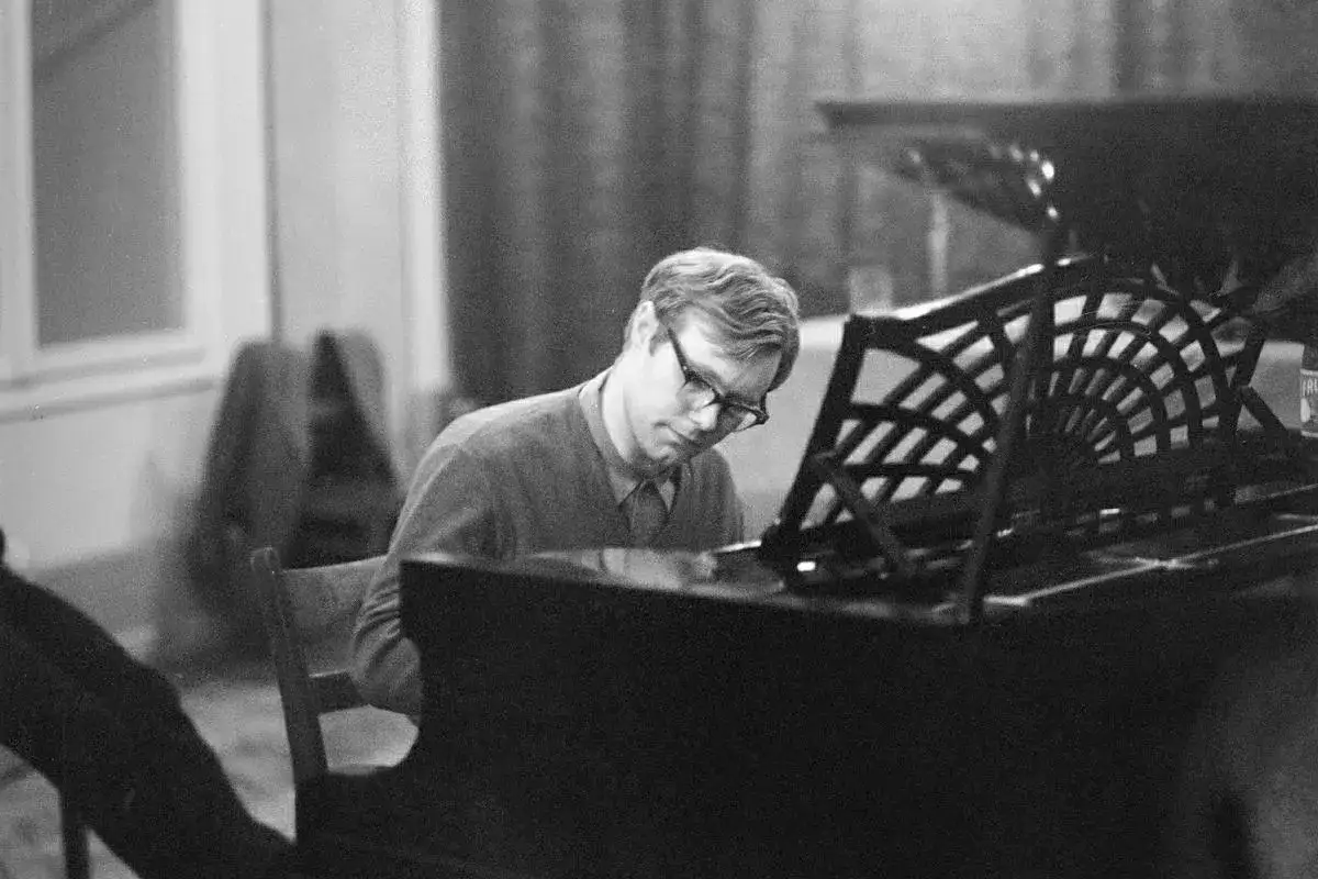 Znany polski kompozytor i pianista jazzowy, Krzysztof Komeda, pochyla się nad fortepianem, pogrążony w tworzeniu muzyki.