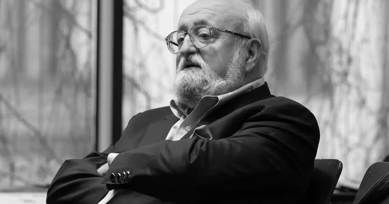 Krzysztof Penderecki w okularach, z siwą brodą, w garniturze, z rękami skrzyżowanymi na piersi.