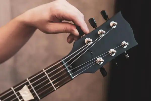 Dłoń kręci kluczem, by nastroić gitarę klasyczną. Idealne brzmienie czeka!
