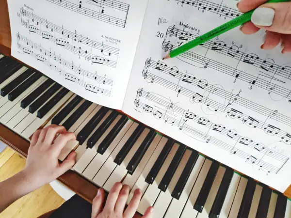Dziecko uczy się grać na pianinie, ćwicząc nuty z podręcznika. Zielony ołówek wskazuje fragment partytury, co ułatwia naukę gry na instrumentach dla dzieci.