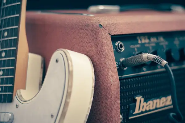 Biała gitara elektryczna podłączona do wzmacniacza Ibanez. Idealny zestaw, by zacząć naukę, jak grać na gitarze elektrycznej.